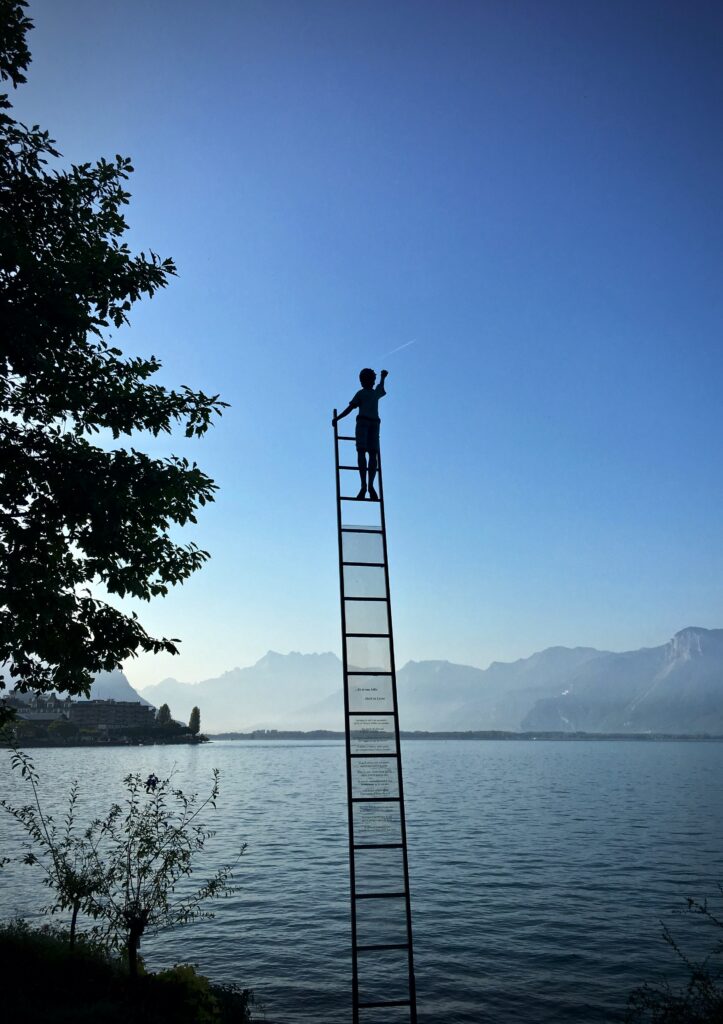 Ein Foto von einem See, in dem eine Leiter zu sehen ist, die ins Nichts führt und ein Junge darauf steht